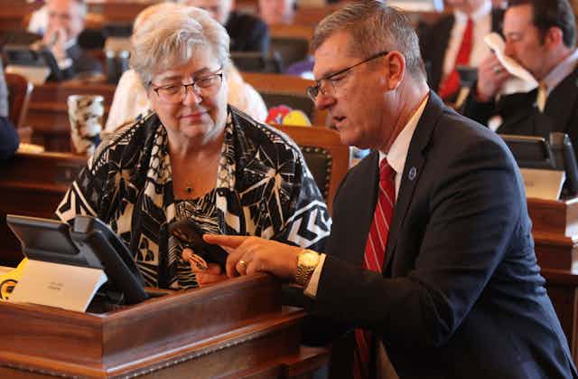 Two people talk while looking at a smartphone.