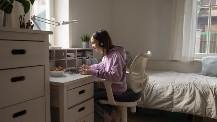 A teenage girl works at her desk in her bedroom.