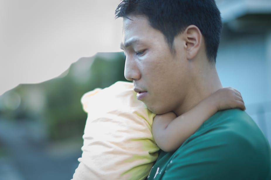 A tired or sad looking young man holds a baby.
