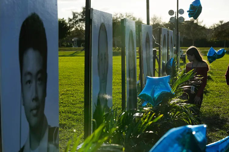 A student sits in front of large portraits of students who were killed in a shooting.