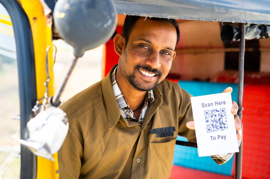 Smiling man holds up card with QR code that says: 'Scan here to pay".