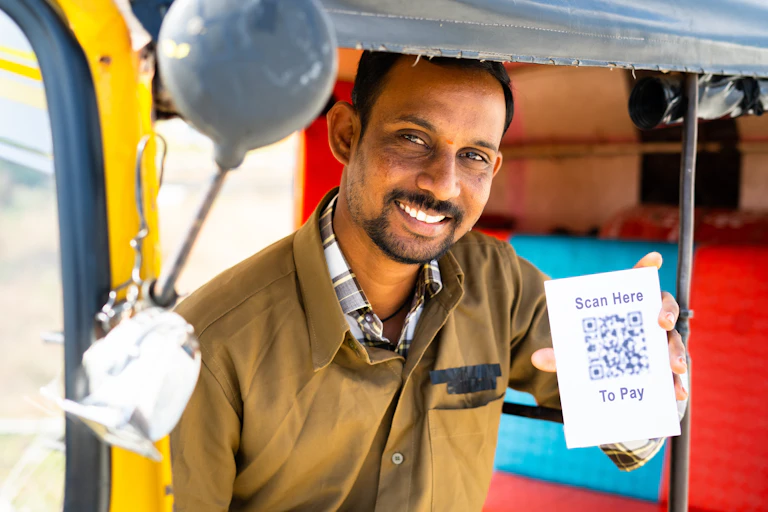 Smiling man holds up card with QR code that says: 'Scan here to pay".