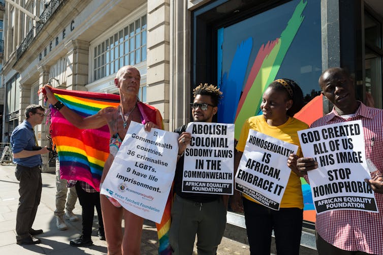 Four people stand outside the Commonwealth headquarters in Central London, carrying pro-LGBTQ+ signs
