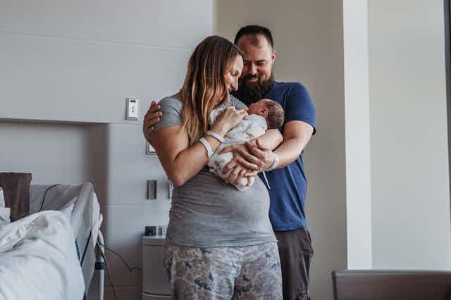 New parents embracing and holding infant in hospital room