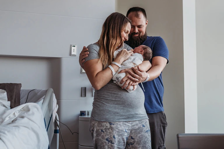 New parents embracing and holding infant in hospital room