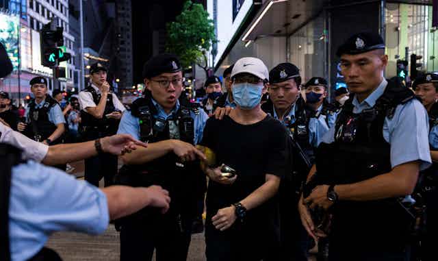 Hong Kong police detain a  Tiananmen Square protestor wearing a COVID mask.