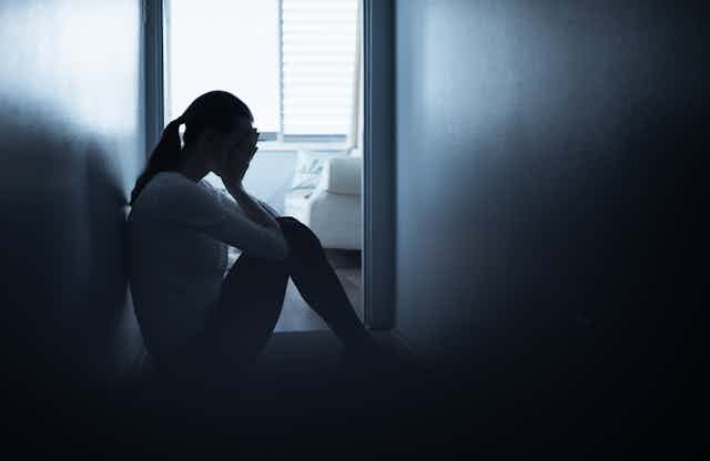 Silhouette of a young woman sitting on the floor in a hallway with her head in her hands