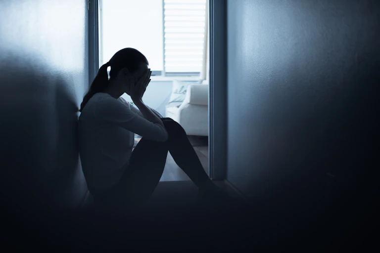 Silhouette of a young woman sitting on the floor in a hallway with her head in her hands