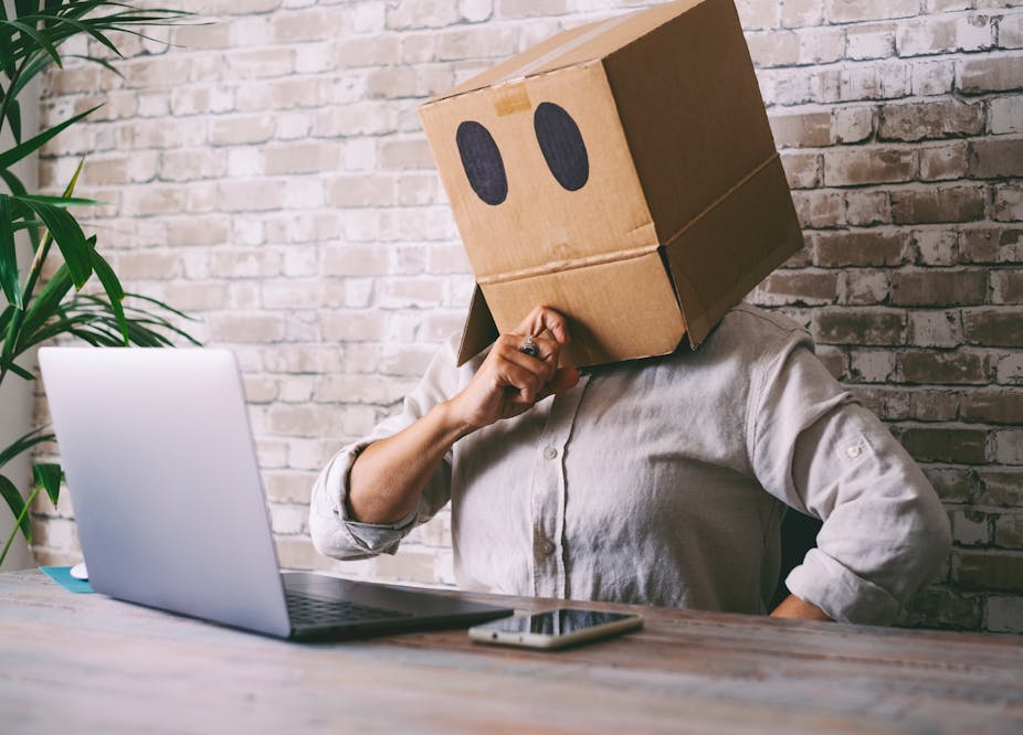 Man looking at his laptop with a cardboard box over his head