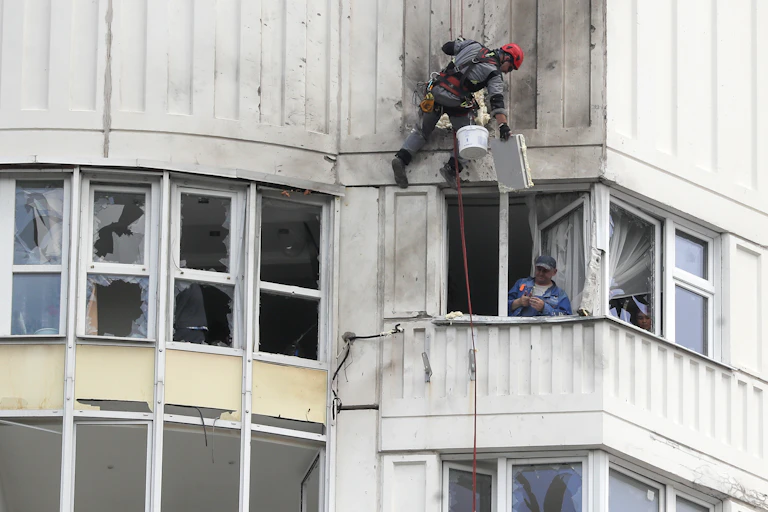 A worker repairs damage to an apartment building in Moscow as the inhabitant looks out.