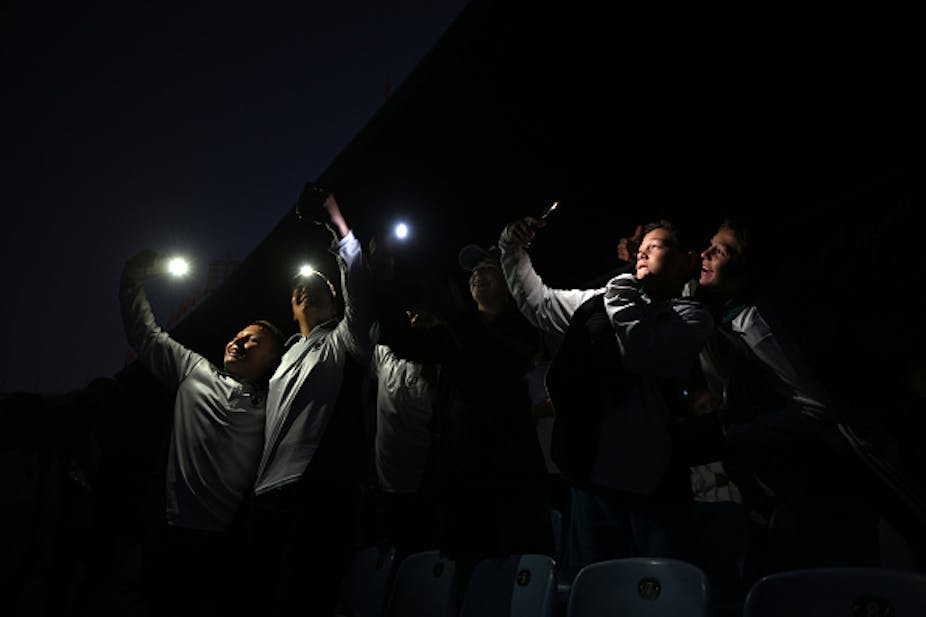 A group of people hold up cellphone torches in the dark.