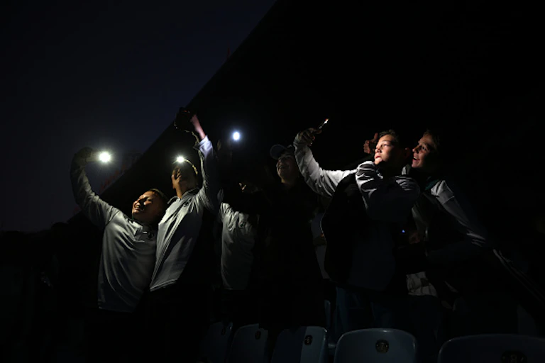 A group of people hold up cellphone torches in the dark.