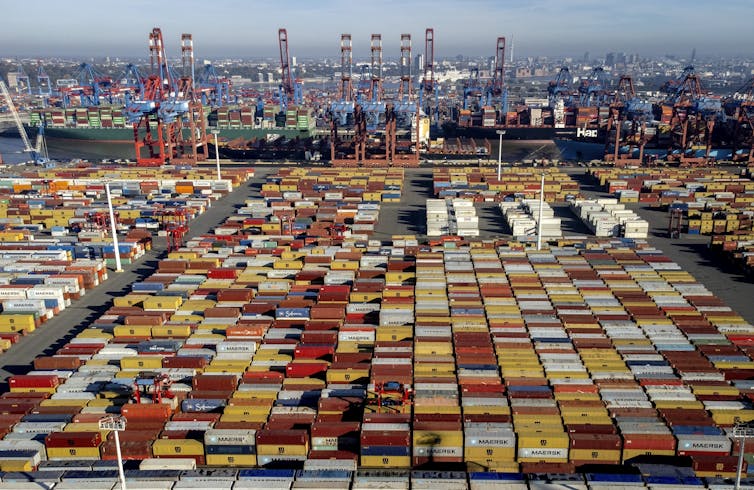 A cargo ship is alongside a pier with ranks of hundreds of shipping containers stacked nearby.