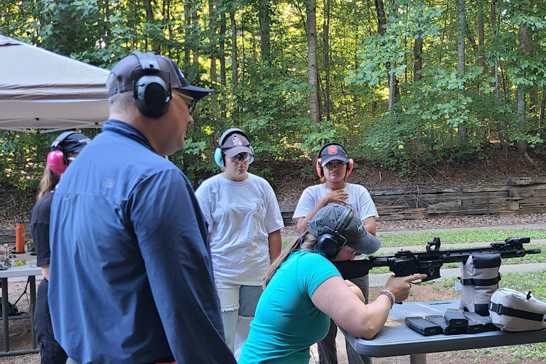 Student shoulders a rifle while professor and fellow students look on.
