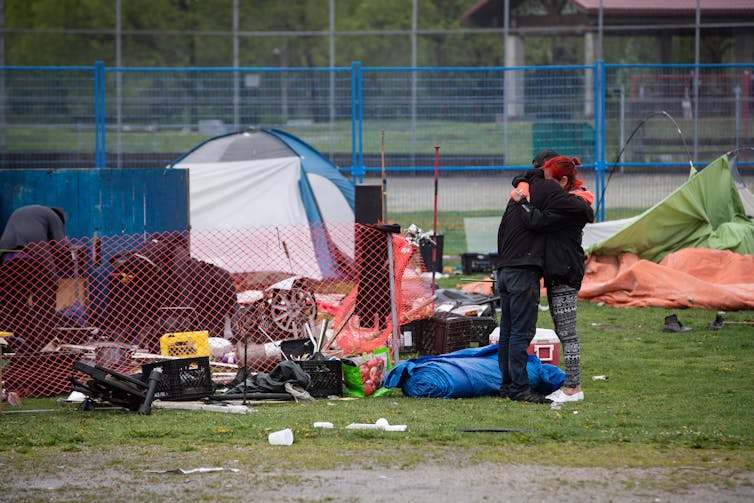 A man and woman hug next to belongings gathers on the ground.
