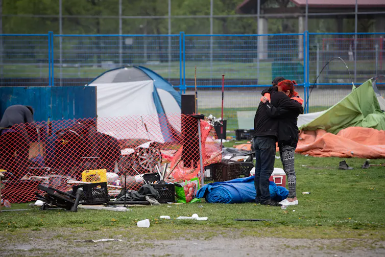 A man and woman hug next to belongings gathers on the ground.