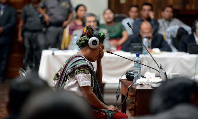 An indigenous woman in headphones in a crowded room, crying.