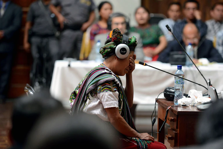 An indigenous woman in headphones in a crowded room, crying.
