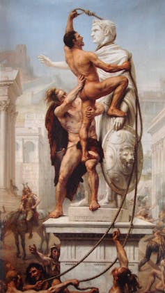 Dos hombres desnudos se encaraman a la estatua de un emperador romano para vandalizarla.