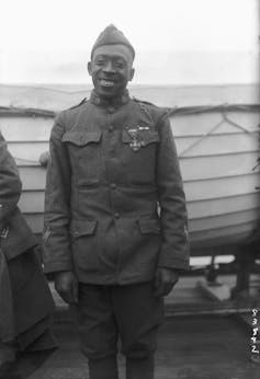 A Black man dressed in a military uniform  is smiling after receiving a medal for bravery.