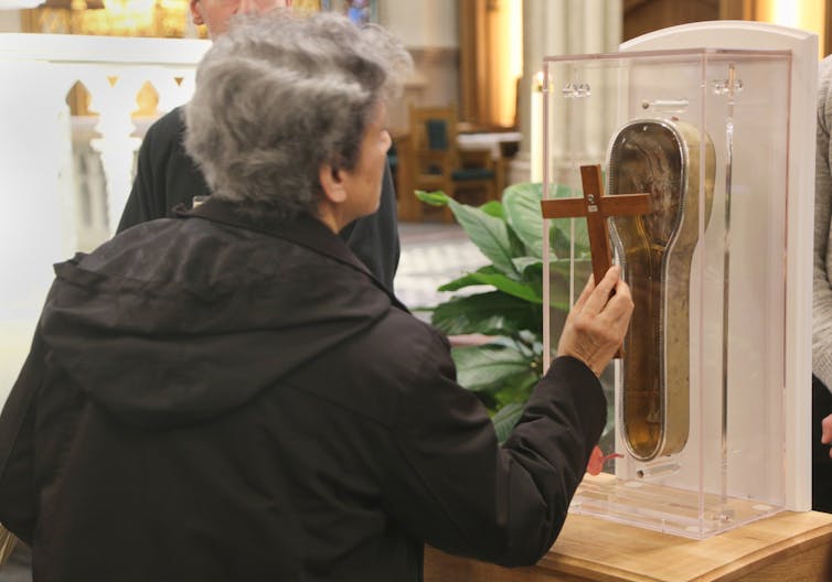 A woman holds the crucifix close to a sacred Catholic relic encased in glass.