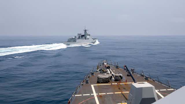 A military vessel is seen crossing into the path of another, white wake behind it.