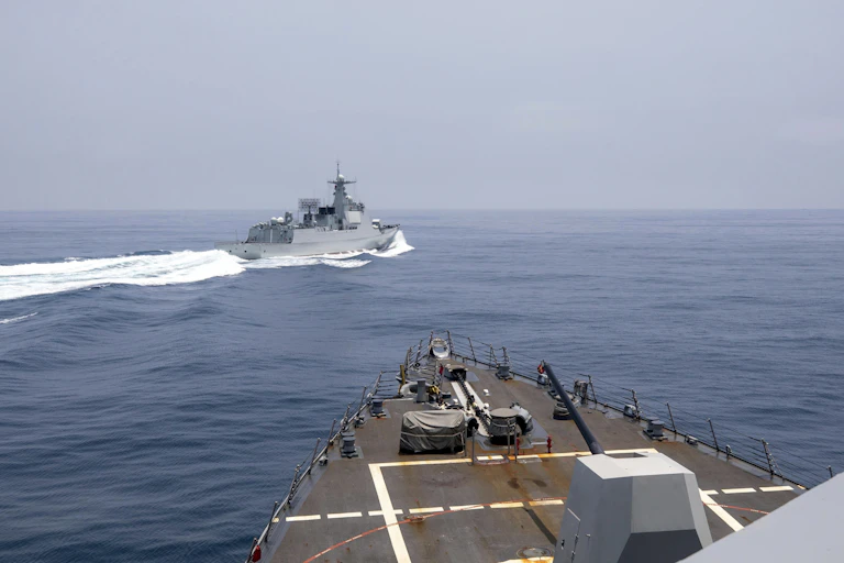 A military vessel is seen crossing into the path of another, white wake behind it.