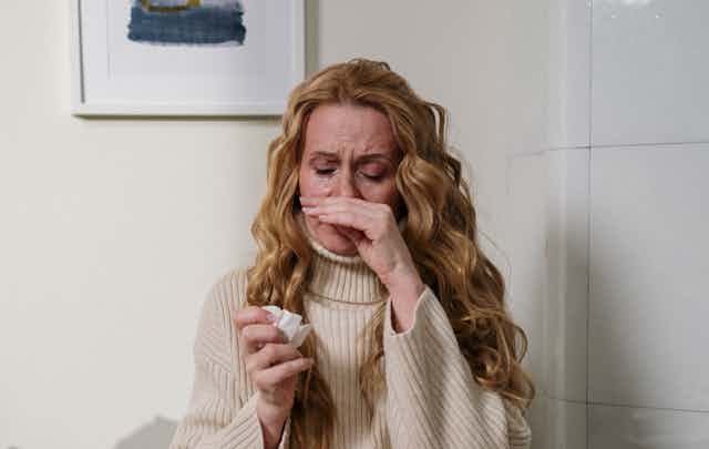 woman rubs nose and holds tissue