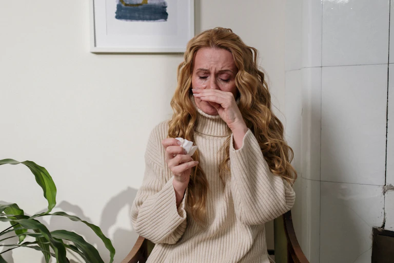 woman rubs nose and holds tissue
