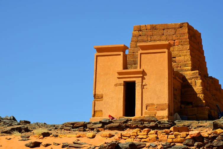 A blocky pyramid of stone with an elegant facade, set against an open blue sky.