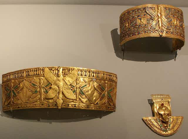 Three pieces of gold, intricately decorated jewelry in a museum display.
