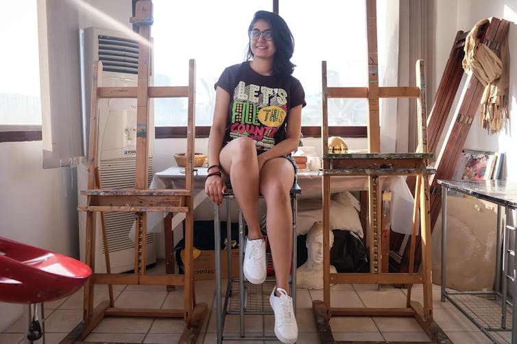 A young girls sits in an art studio.