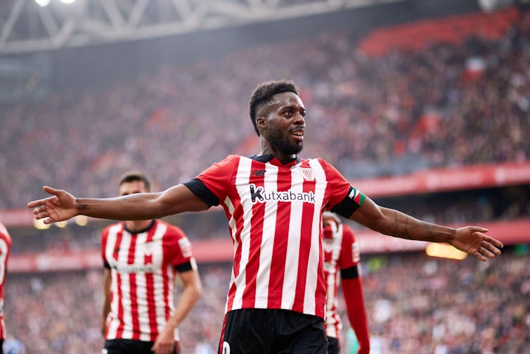 A footballer in a red and white kit celebrates a goal.