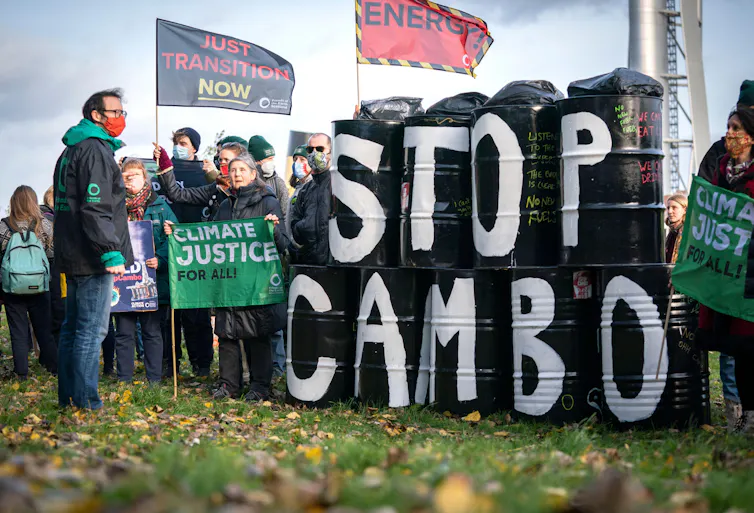 Campaigners hold flags and stand beside black barrels painted with the message 'stop Cambo'.
