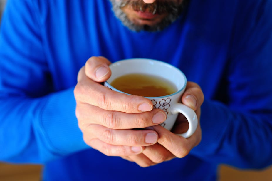 A middle-aged man holds a cup of green team in his hands.