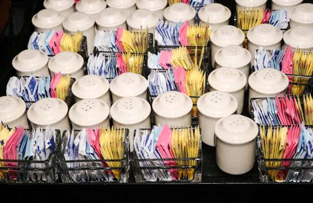 Food service tray holding rows of artificial sugar packets and salt and pepper shakers.