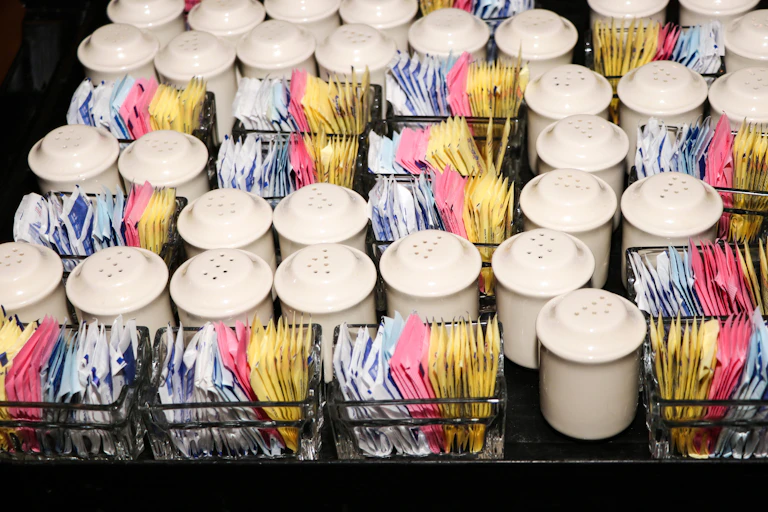 Food service tray holding rows of artificial sugar packets and salt and pepper shakers.