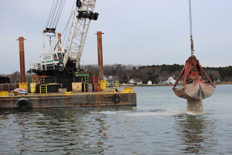 A dredge deposits crushed shells off a floating platform.