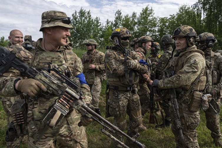 Men in battle fatigues carrying large weapons smile and chat.