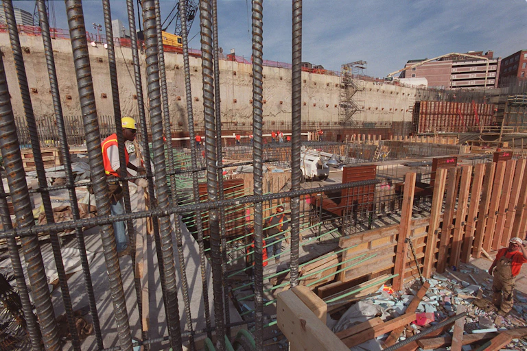 Workers stand on platforms in a large concrete opening filled with beams