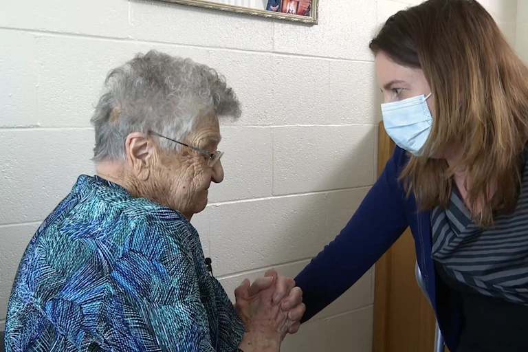 An older woman in a blue dress with a younger woman wearing a face mask
