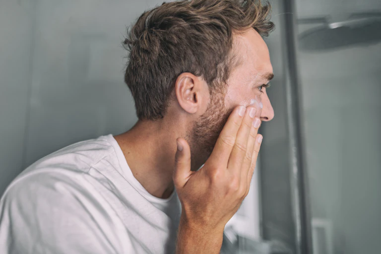 man puts cream on face in mirror
