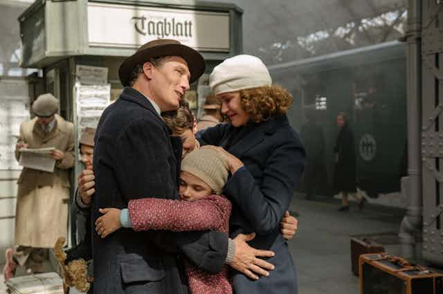 Un hombre, una mujer, un niño y una niña se abrazan en el andén de una estación de tren.