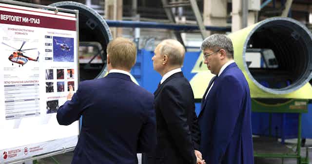 Vladimir Putin and two men look at a diagram of a helicopter at a factory in March 2023.