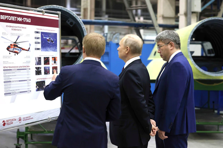 Vladimir Putin and two men look at a diagram of a helicopter at a factory in March 2023.