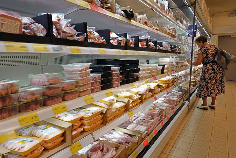 Woman looks at refridgerated shelves of meat in a supermarket.