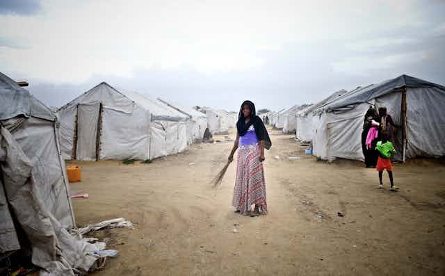 Woman holding a broom while standing in front of a row of tents.
