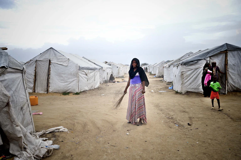 Woman holding a broom while standing in front of a row of tents.