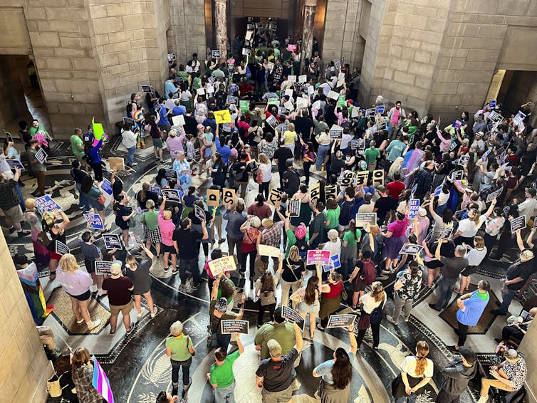 Crowd of protesters holding signs in a legislative building