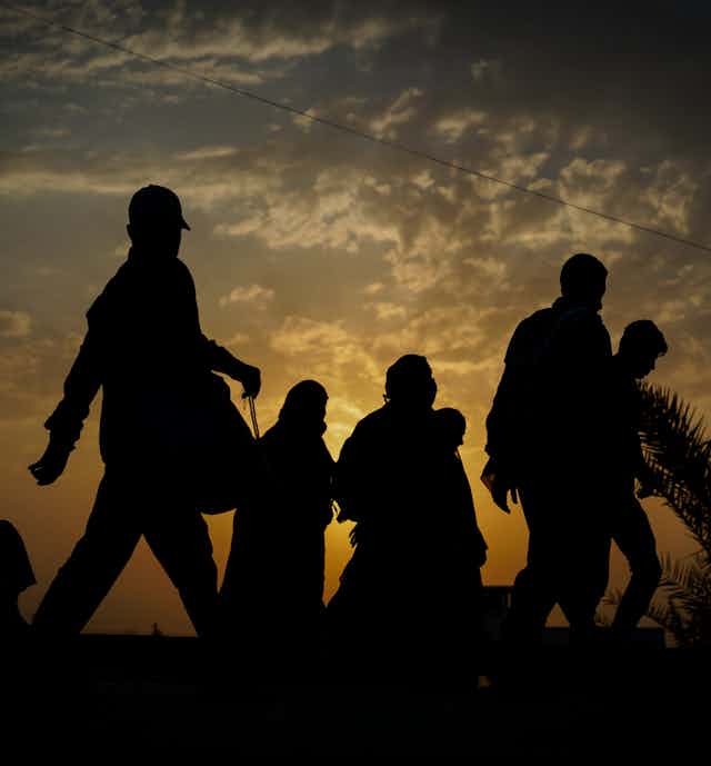 Silhouetted against a fading sunset, a group of immigrants walk with their belongings.